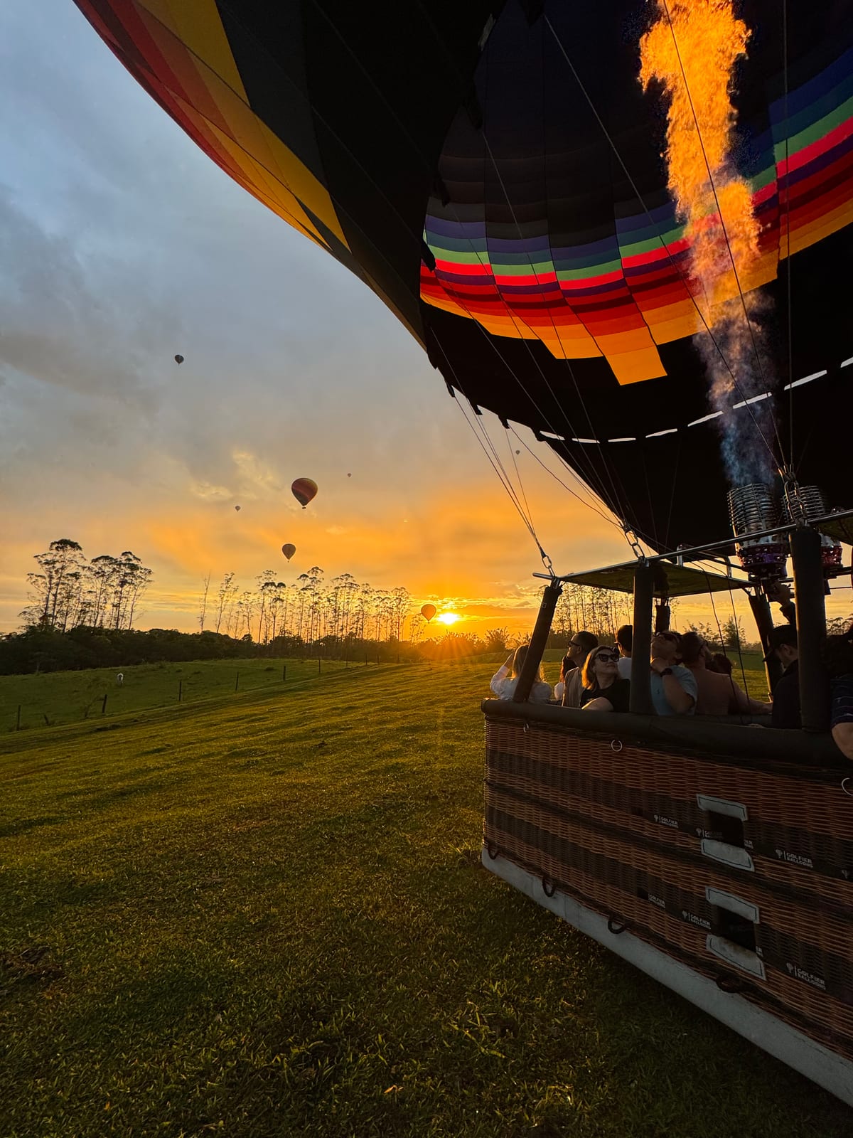 Cesto com passageiros decolando ao amanhecer, com outros balões ao longe no horizonte